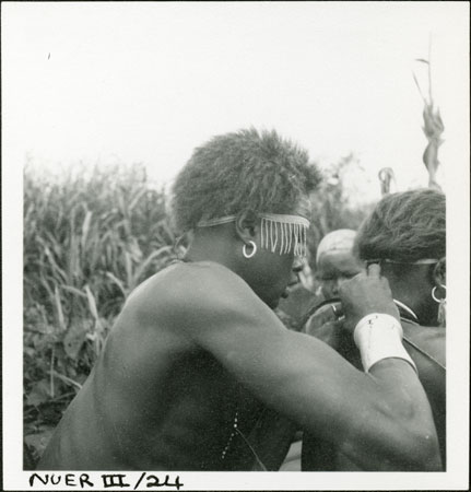 Nuer youth tying necklace