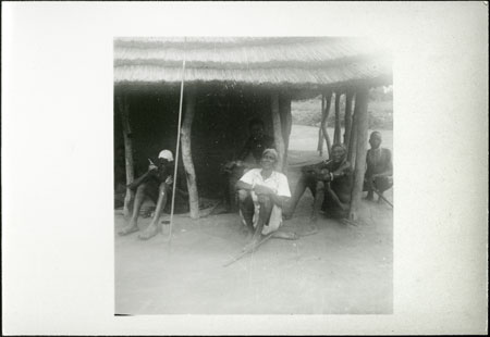 Mandari men sitting outside hut